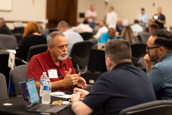 Trucking fleet manager talks across small table to two supplier hosts at HDTX
