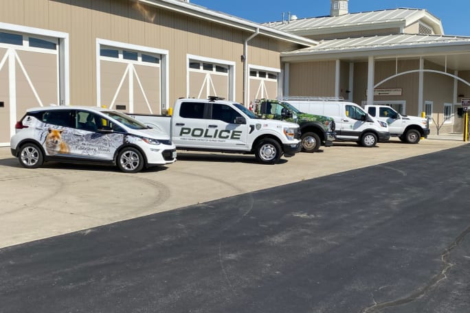 A lineup of alt-fuel vehicles is shown in front of a fleet shop. (from left) Chevy Bolt, Ford F-150 Powerboost Hybrid, Ford F-450 that runs on propane, Ford E-Transit van, and Ford F-150 Lightning.