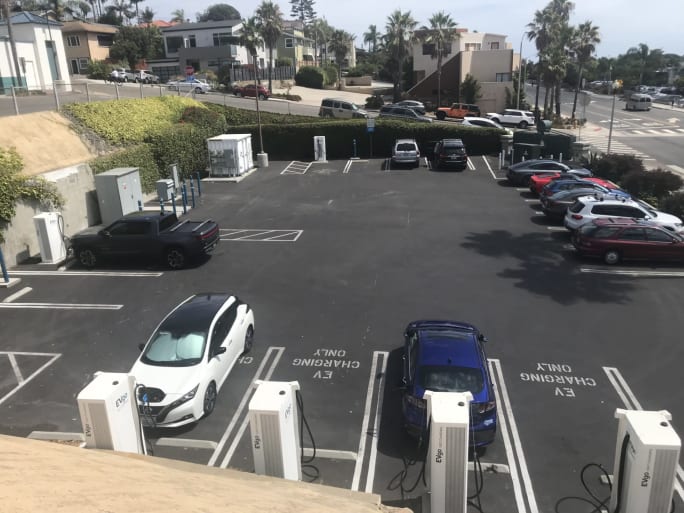 Overview photo of the finished charging depot in Encinitas, California, with chargers lined up on a smooth parking surface with a large generator situated in a far corner of the parking lot.