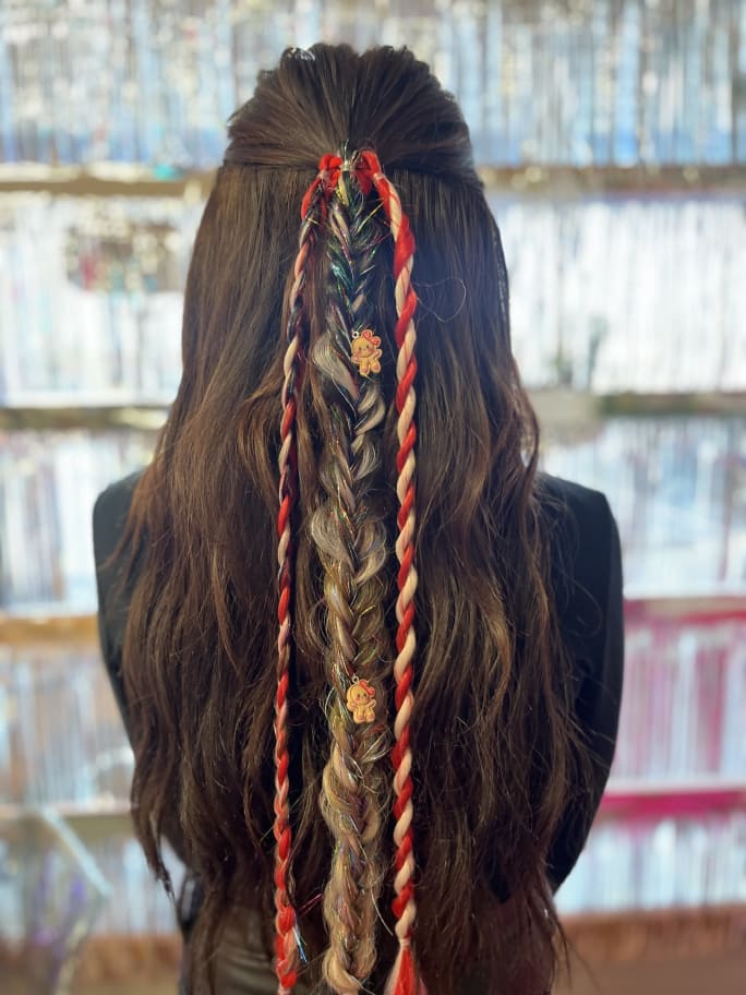 The back of a brunette's head, showing long tresses with red and tinsel braiding with holiday charms.