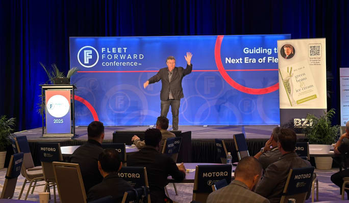 Bill Sims on stage next to an enlarged placard of his book, 