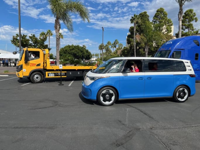 A flatbed truck, a semi, and a VW bus in a parking lot at a ride and drive event.