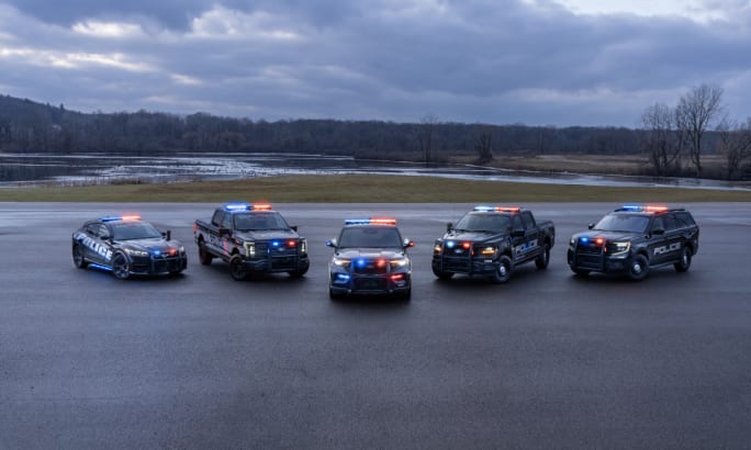 A lineup of five black Ford police vehicles are shown with their lights flashing.
