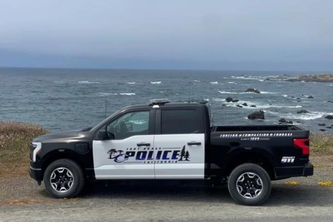 A black Ford F-150 Lightning Pro SSV with white doors and the Fort Brag PD logo is shown sitting in front of the ocean.