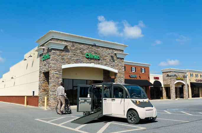 White GEM Wheelchair Accessible Vehicle parked in a handicap space with ramp extended and wheelchair user.