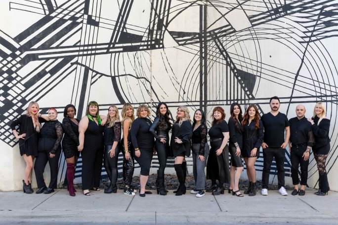 Dressed in black, the team from Harlow Beauty pose in front of a black and white mural on a building.