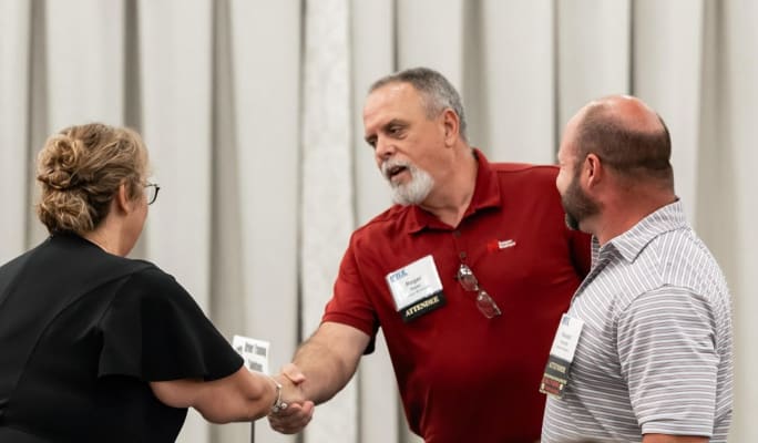 Man in red shirt shaking hands with woman as another man looks on
