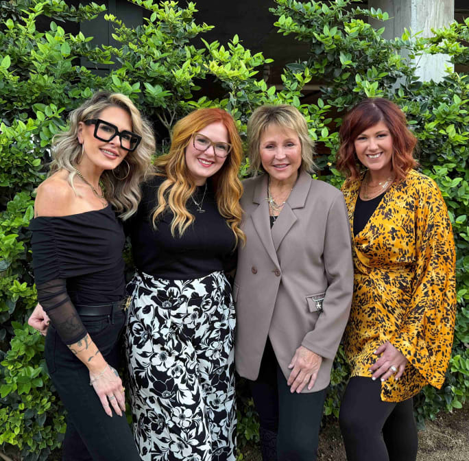 Four women elegantly dressed in front of a tree.