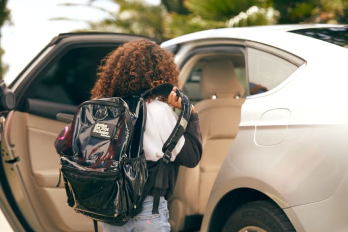 a girl with a backpack steps into a car