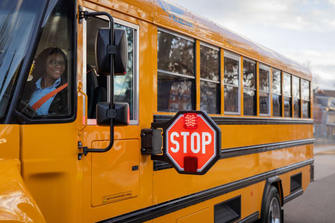 a woman sits in the drivers seat of a school bus with its stop arm out