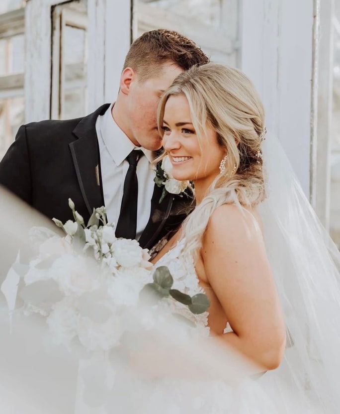 A groom kisses a blonde, smiling bride