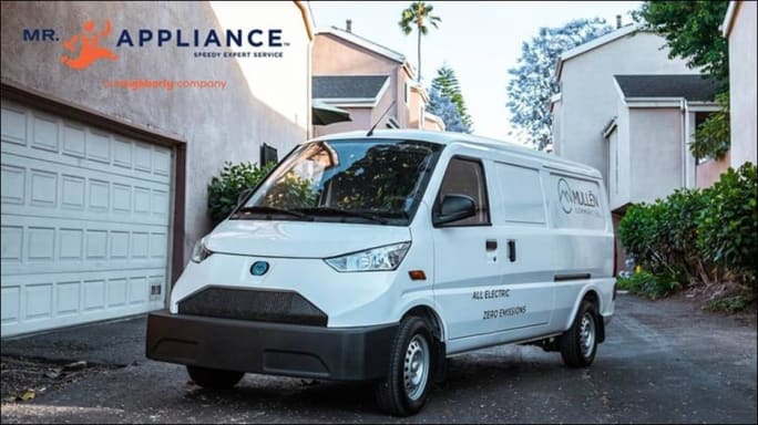 A Mullen Automotive van parked near houses.