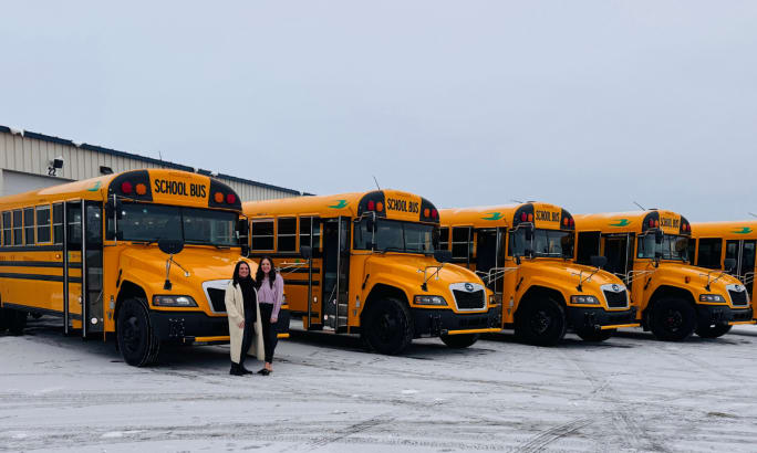 Two women pose in front of five Blue Bird propane buses.