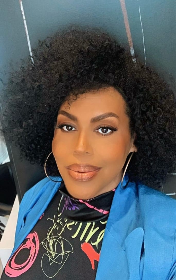 A woman with an afro textured hairstyle in a blue jacket.
