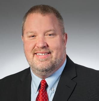 A business portrait of a man in a dark suit with a red tie.