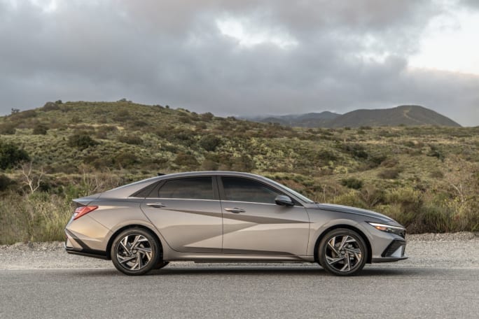 A gold 2025 Hyundai Elantra parked on the side of the road with mountains in background.