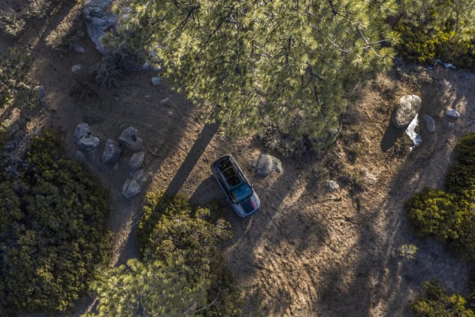 Aerial view of a 2025 Jeep Compass Trailhawk driving on a dirt road in a forest.