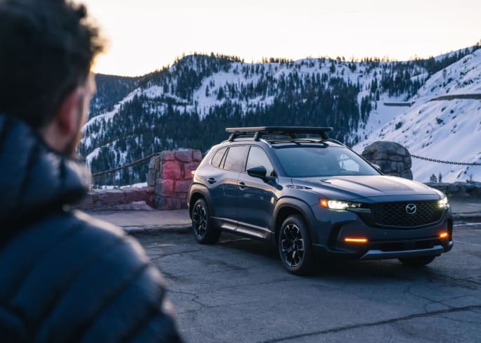 A blue Mazda SUV parked at an overlook of snowy mountains.