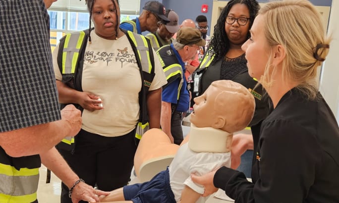 School bus drivers look on as a nurse trains them on first aid using a dummy.
