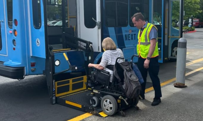 A TriMet NEXT driver helping a wheelchair-bound rider onto the bus via charlift.