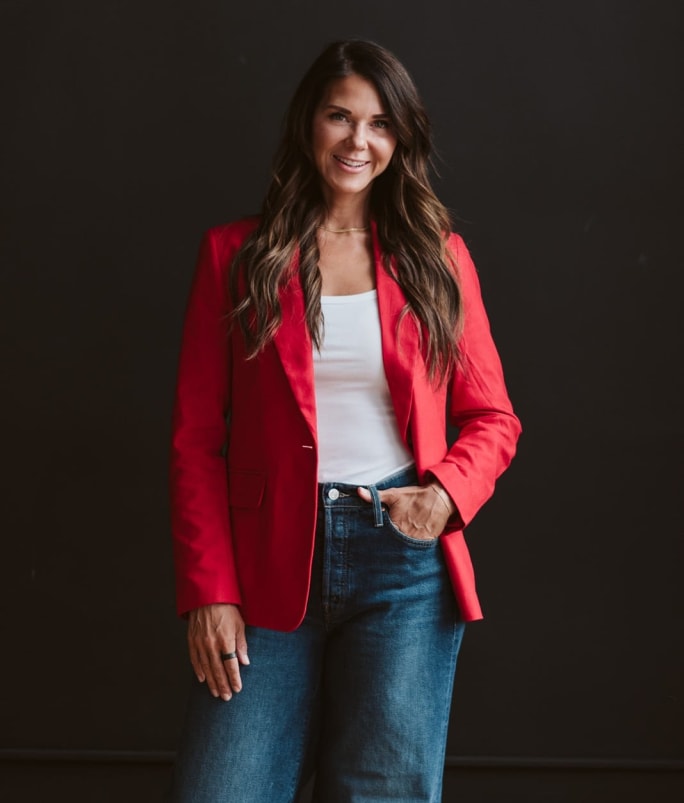 Salon industry leader Kati Whitledge standing confidently in a red blazer, representing innovation, leadership, and data-driven strategies for improving client retention.