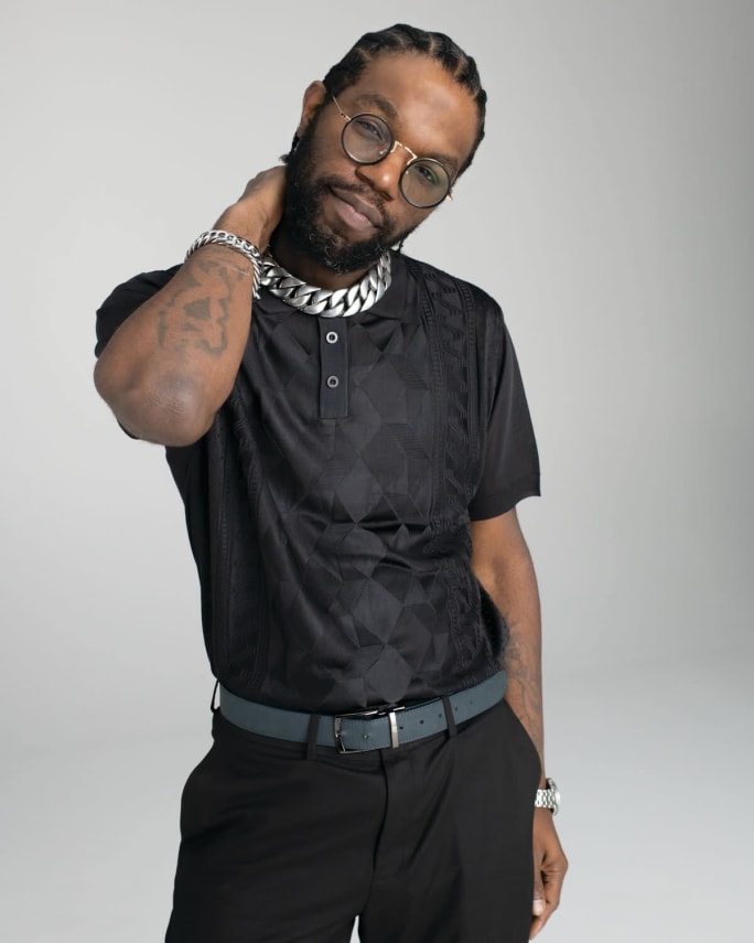A man wearing all black, his hand to his neck.