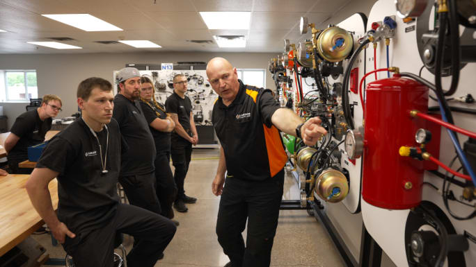 Diesel academy instructor points to items on an air board, speaking to students