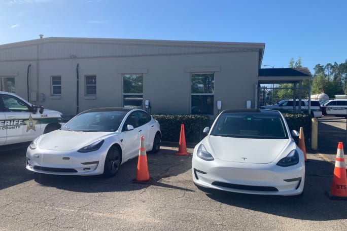 Two white unmarked Tesla 3s sit side by side in a parking lot.