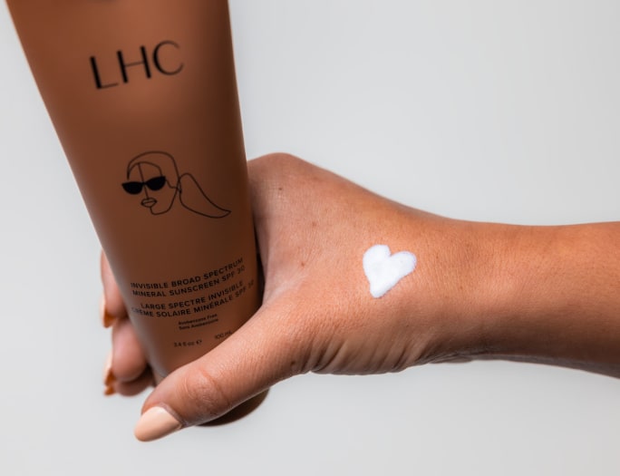 a hand with a sunscreen heart holding a bottle of LHC sunscreen