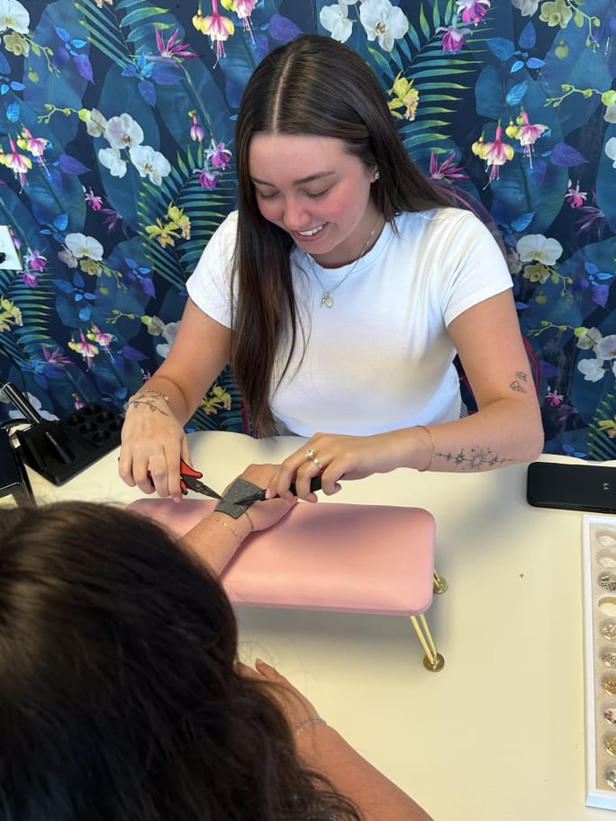 A smiling stylist uses pliers to attach a bracelet to a client's wrist.