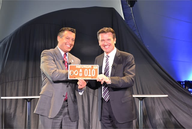 Two men in suits at podium showing off the autonomous license plate