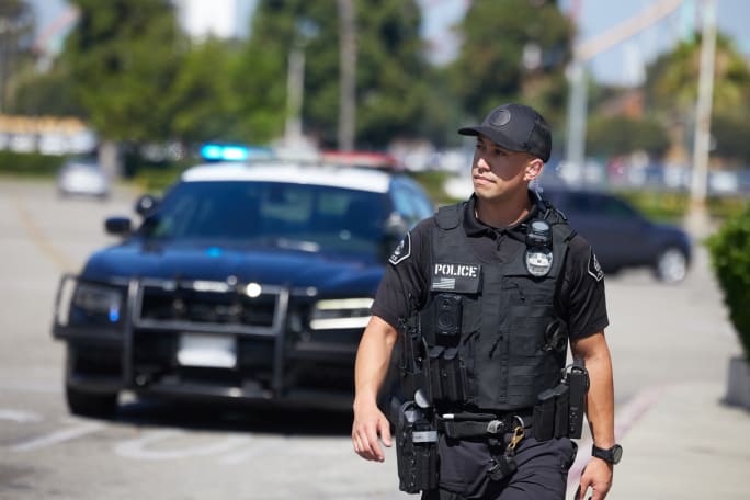 Police officer in tactical gear standing near patrol car on city street