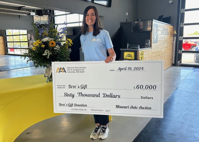 A woman in a light blue shirt poses with a check made out to Bree's Gift for $60,000.