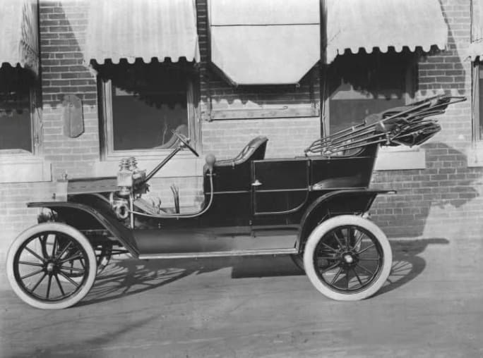Early Ford Model T parked outside a brick building, representing the rise of mass production and America’s automotive beginnings.