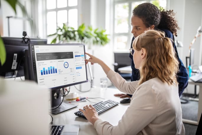 Two colleagues reviewing fleet expense data and charts on a desktop screen in an office setting