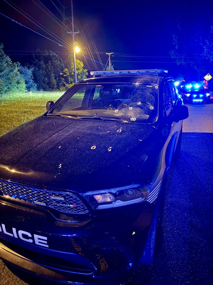 Bullet-riddled police SUV at night with blue emergency lights in background