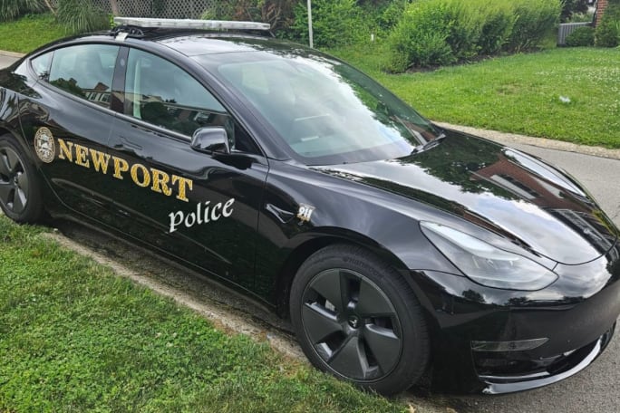 A black Tesla Model 3 with a decal that says 'Newport Police' is parked.