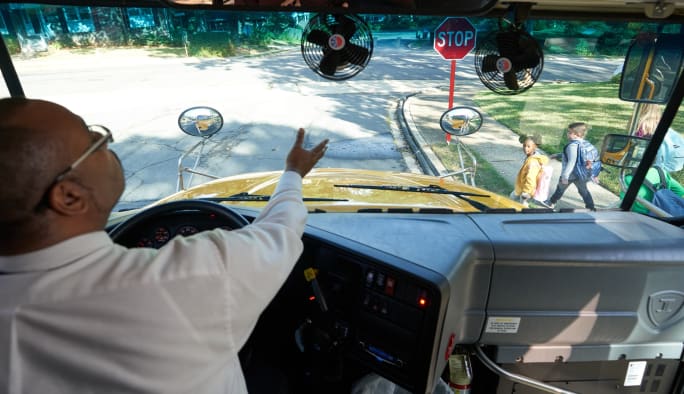 a school bus driver waves kids across the street from the driver's seat