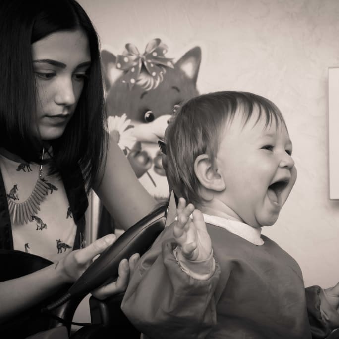 A young female stylist works on a baby in their salon chair.