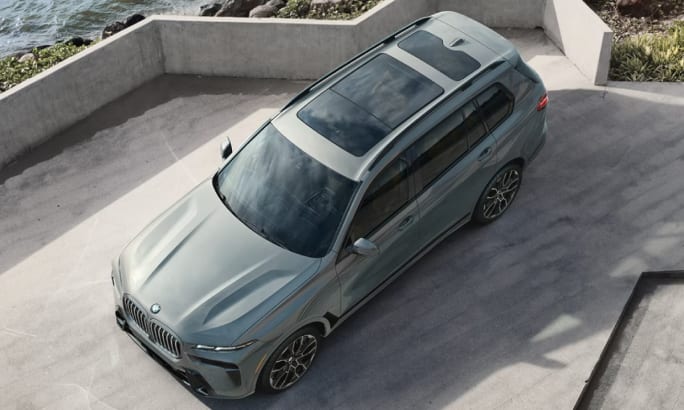 An aerial view of a mint green 2025 BMW X7 on gray pavement.