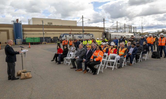A presenter addresses a crowd of people outside.