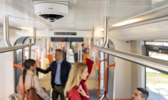 A camera inside a public transit vehicle while riders stand in background.