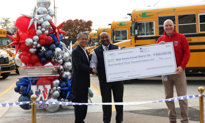 Three people hold up a ComEd check for $930,000 in front of a electric school bus line up.