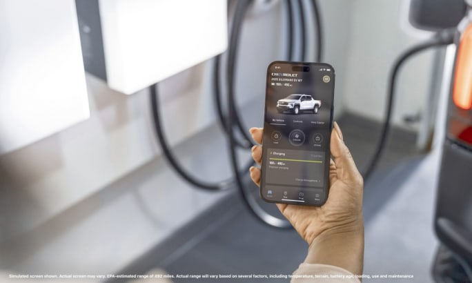 A hand holding a phone showing the charging status of a 2025 Chevrolet Silverado EV.