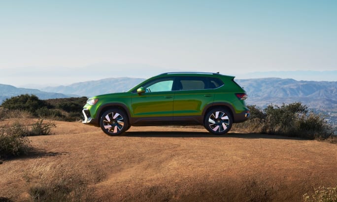 Left exterior angle of a bright green 2025 Volkswagen Taos parked on a dirt road with mountains in the background.