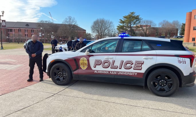 Alabama A&M University electric police SUV with emergency lights activated parked on campus with officers standing nearby.