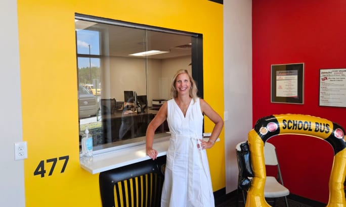a woman stands at a front desk painted like a school bus