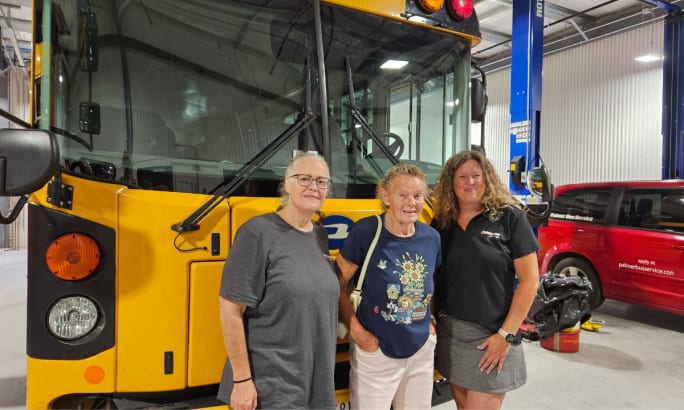 three women stand in front of a school bus