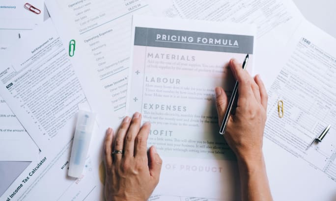 Human hands working on a spread of work papers on a desk focused on pricing.