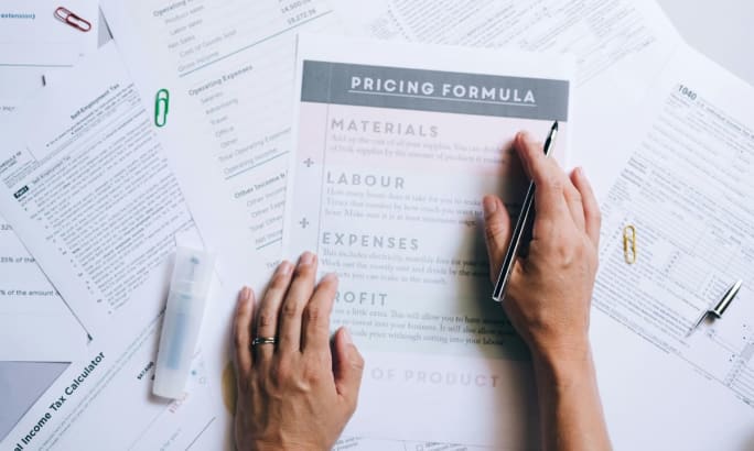 Human hands working on a spread of work papers on a desk focused on pricing.